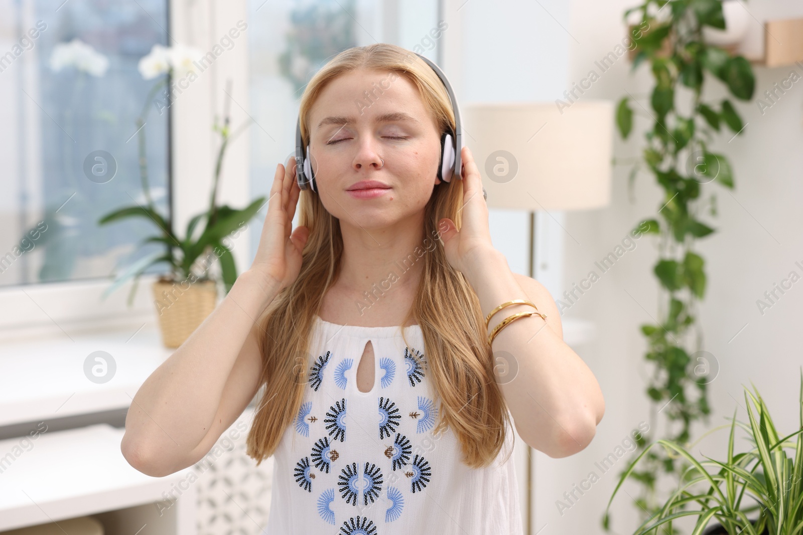 Photo of Feng shui. Young woman in headphones listening to music near houseplants at home