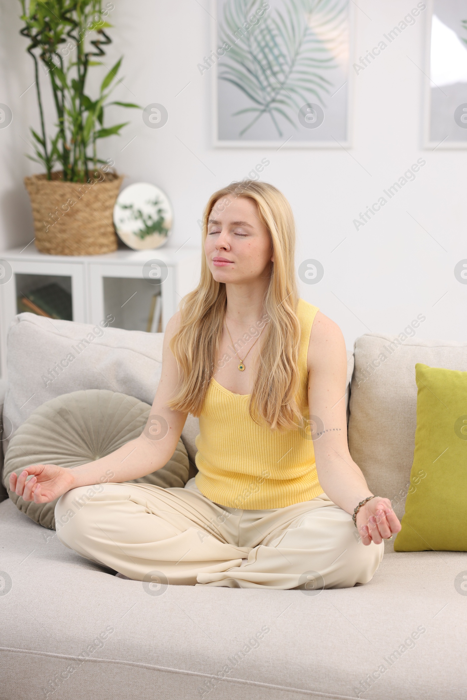 Photo of Feng shui. Young woman meditating on couch at home