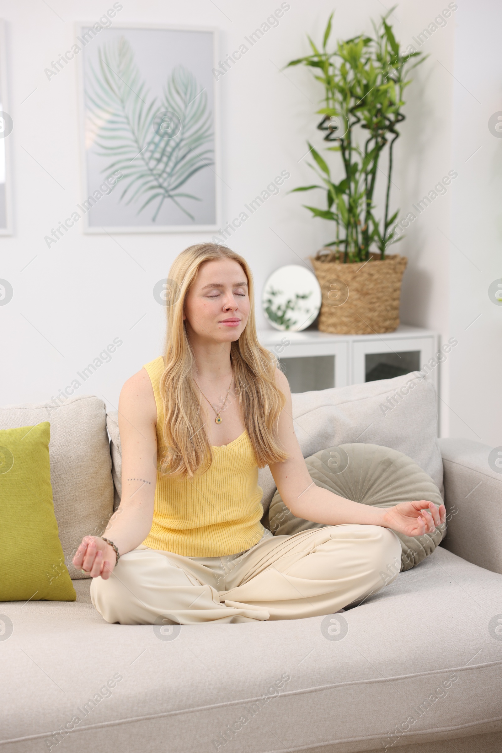 Photo of Feng shui. Young woman meditating on couch at home