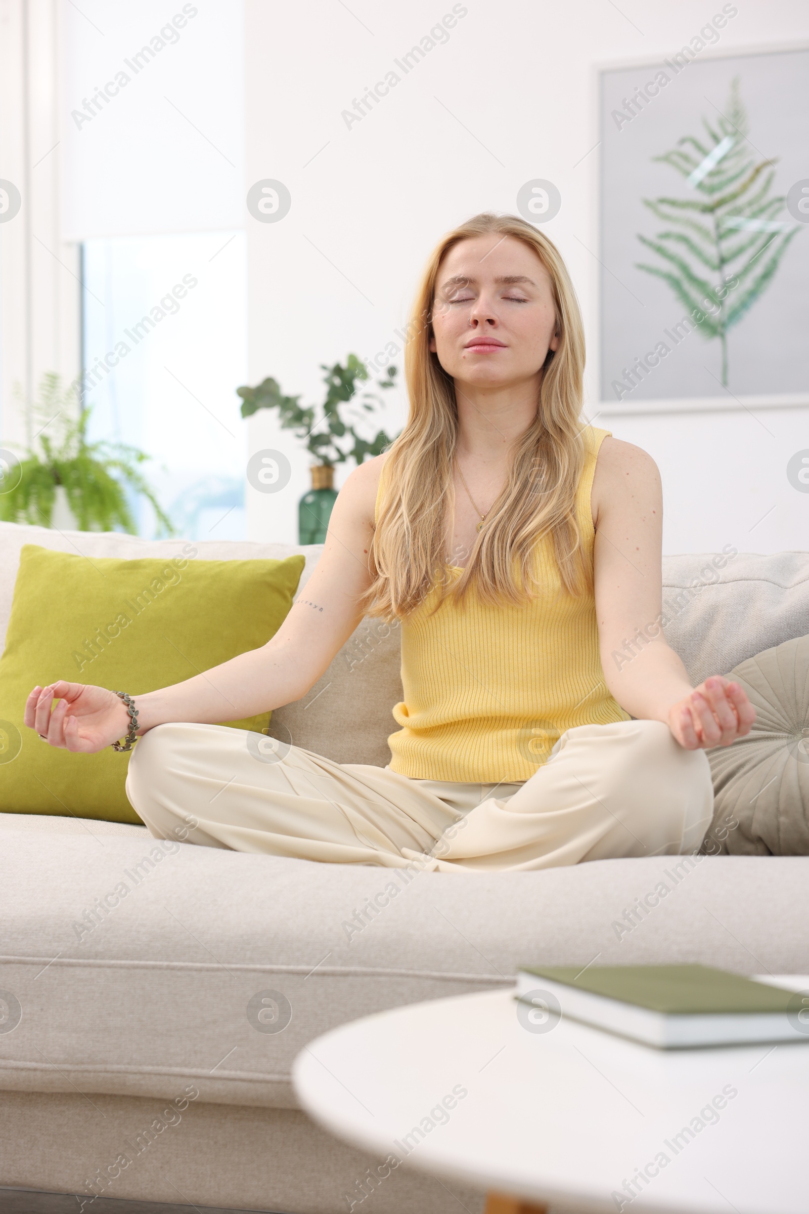 Photo of Feng shui. Young woman meditating on couch at home