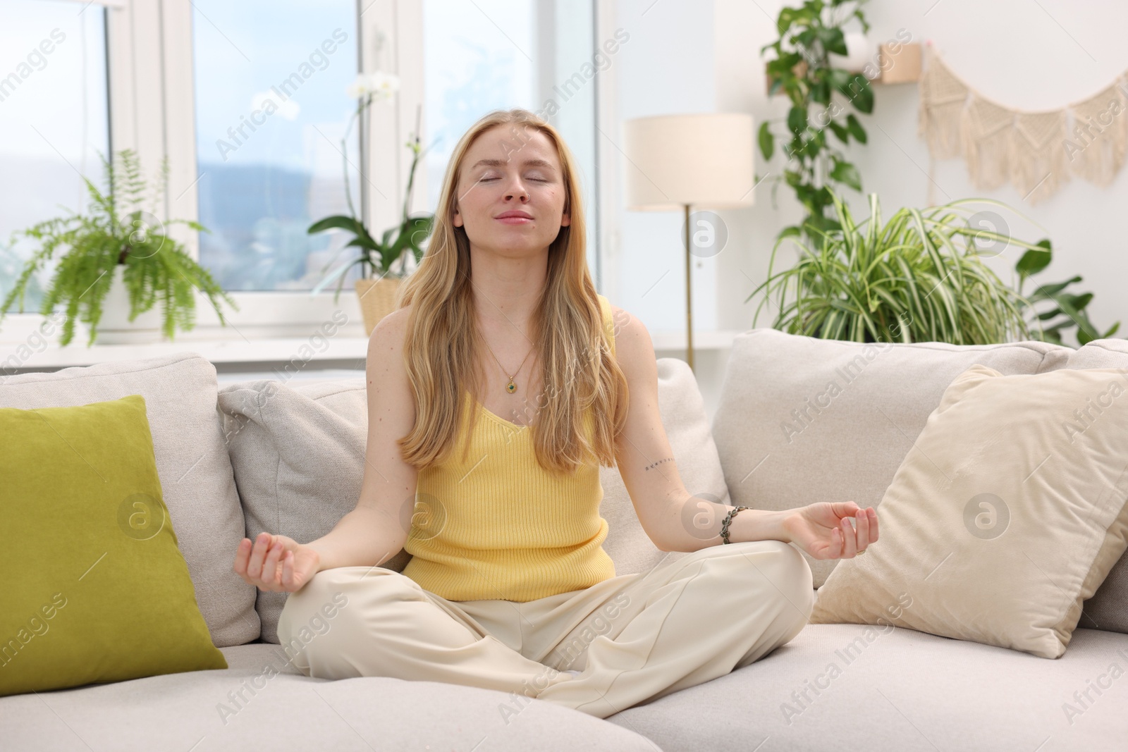 Photo of Feng shui. Young woman meditating on couch at home