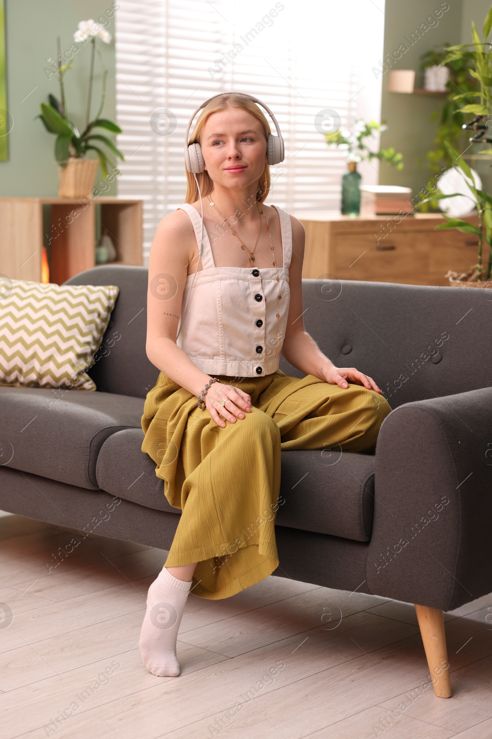 Photo of Feng shui. Young woman with headphones sitting on couch at home