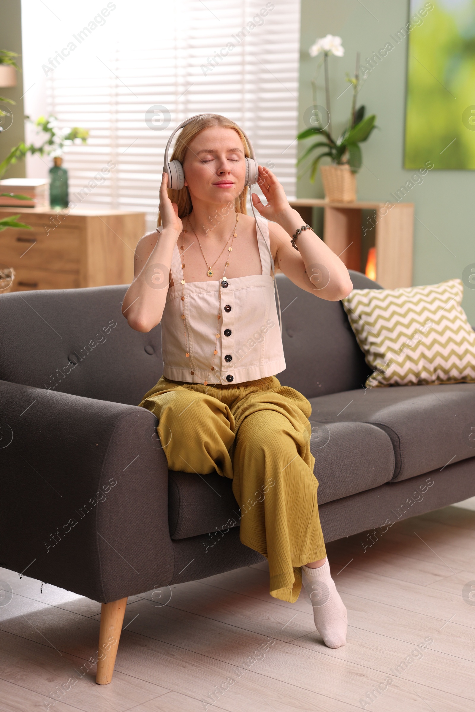 Photo of Feng shui. Young woman with headphones sitting on couch at home