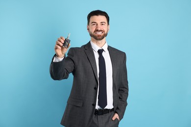 Photo of Cheerful salesman with car key on light blue background