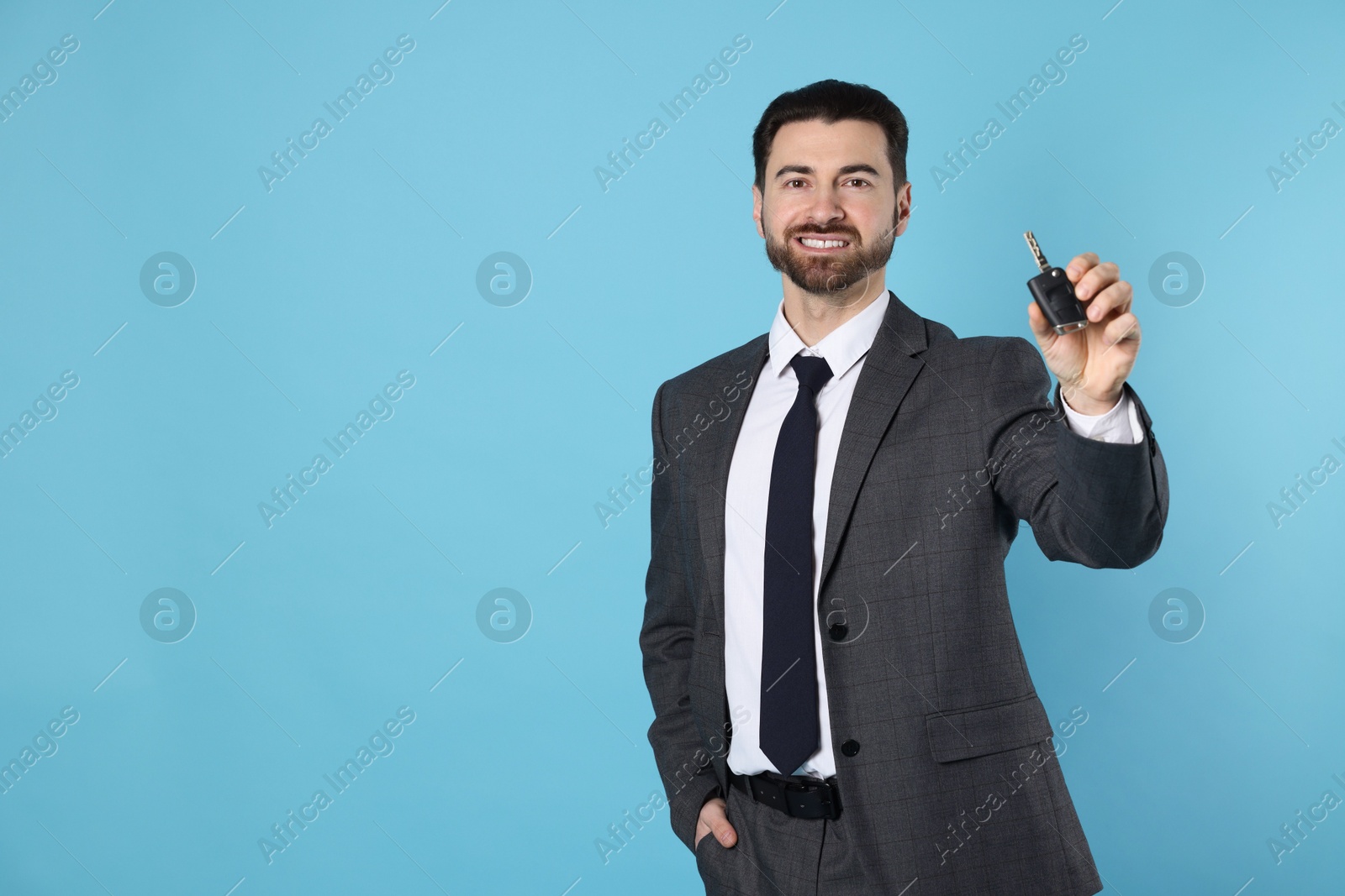 Photo of Cheerful salesman with car key on light blue background