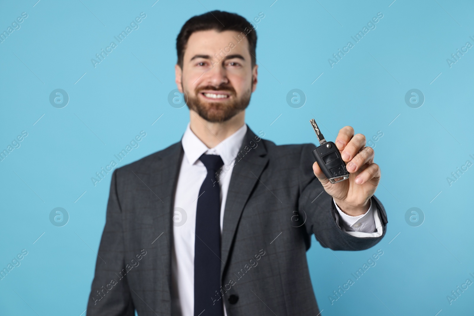 Photo of Cheerful salesman with car key on light blue background, selective focus