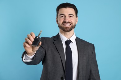 Photo of Cheerful salesman with car key on light blue background