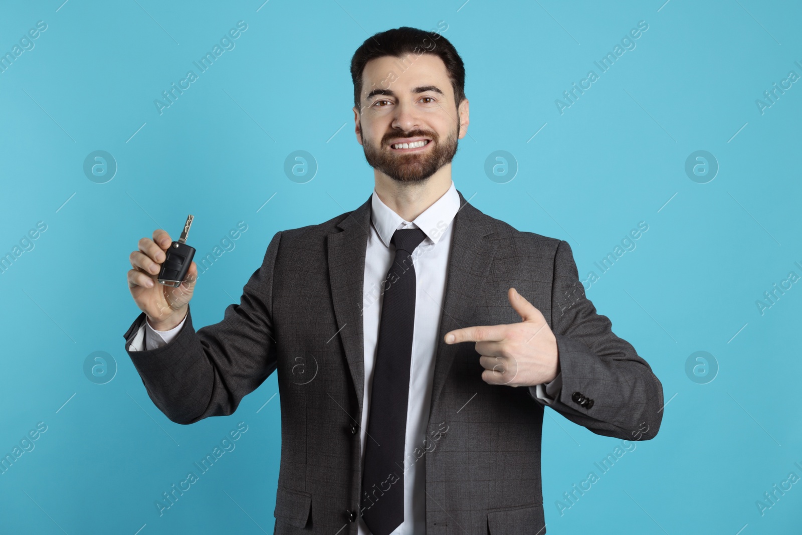 Photo of Cheerful salesman pointing at car key on light blue background