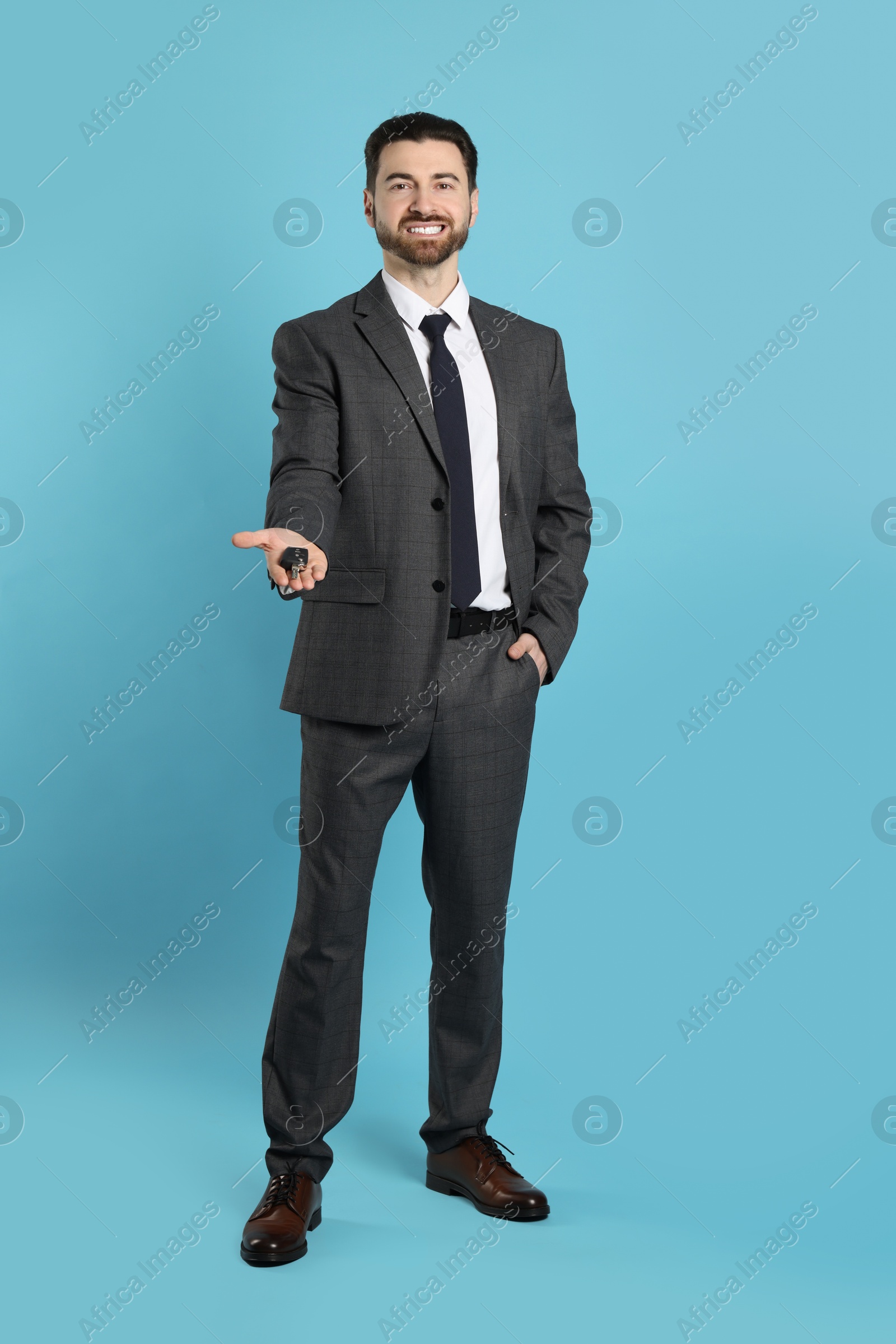 Photo of Cheerful salesman with car key on light blue background