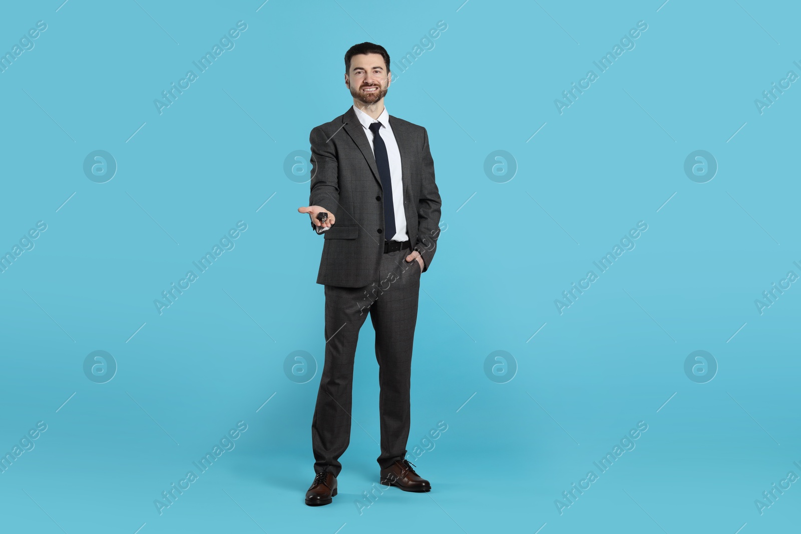 Photo of Cheerful salesman with car key on light blue background