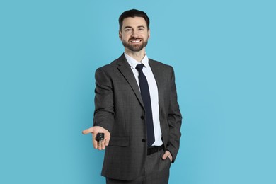 Photo of Cheerful salesman with car key on light blue background