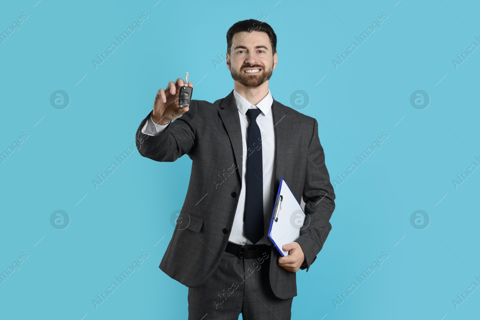 Photo of Cheerful salesman with car key and clipboard on light blue background