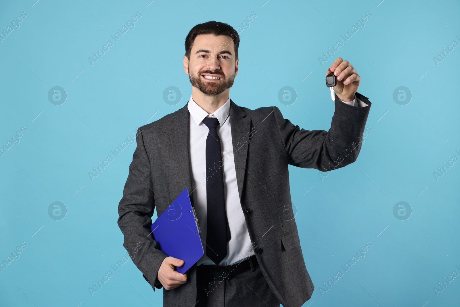 Photo of Cheerful salesman with car key and clipboard on light blue background