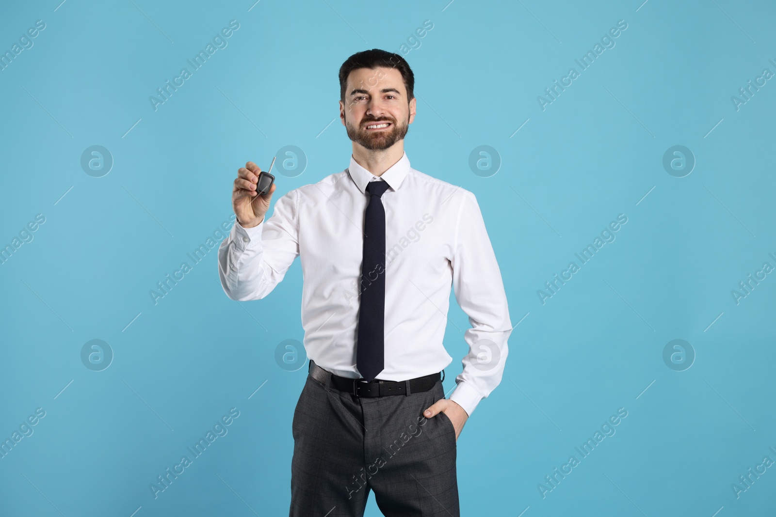 Photo of Cheerful salesman with car key on light blue background