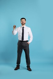 Photo of Cheerful salesman with car key on light blue background