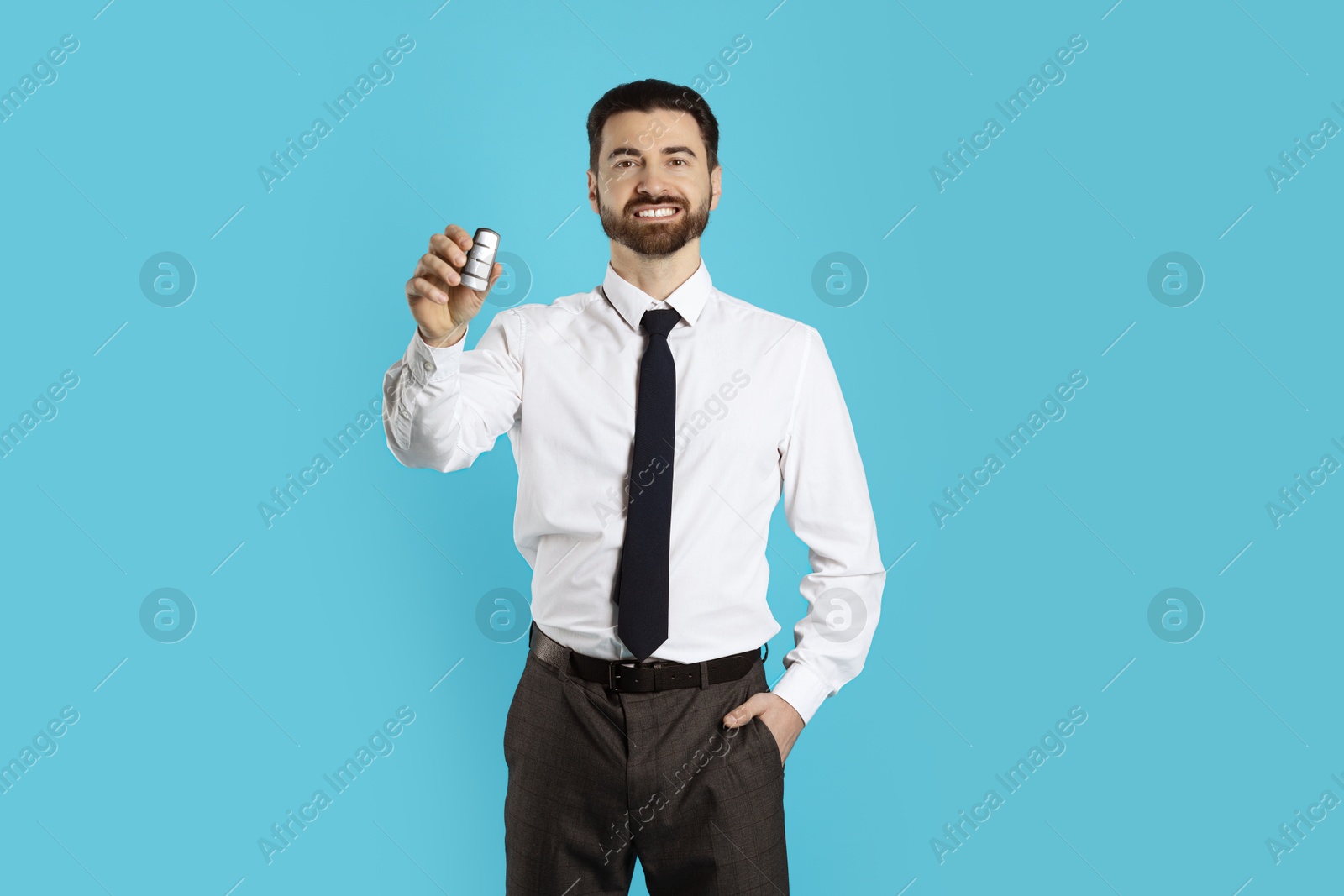 Photo of Cheerful salesman with car key on light blue background