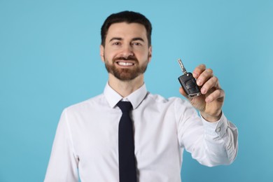 Photo of Cheerful salesman with car key on light blue background, selective focus