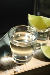 Tequila shots, slices of lime, salt and agave leaf on wooden table against black background, closeup