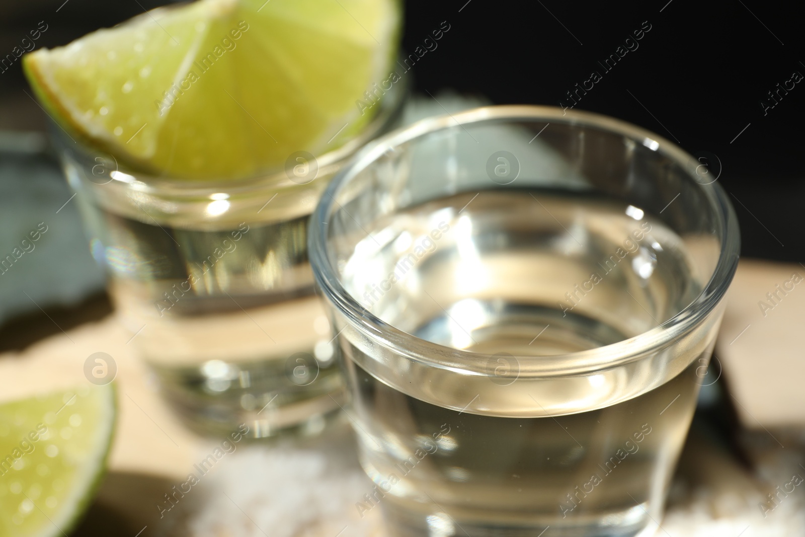 Photo of Tequila shots and slices of lime on table against black background, closeup