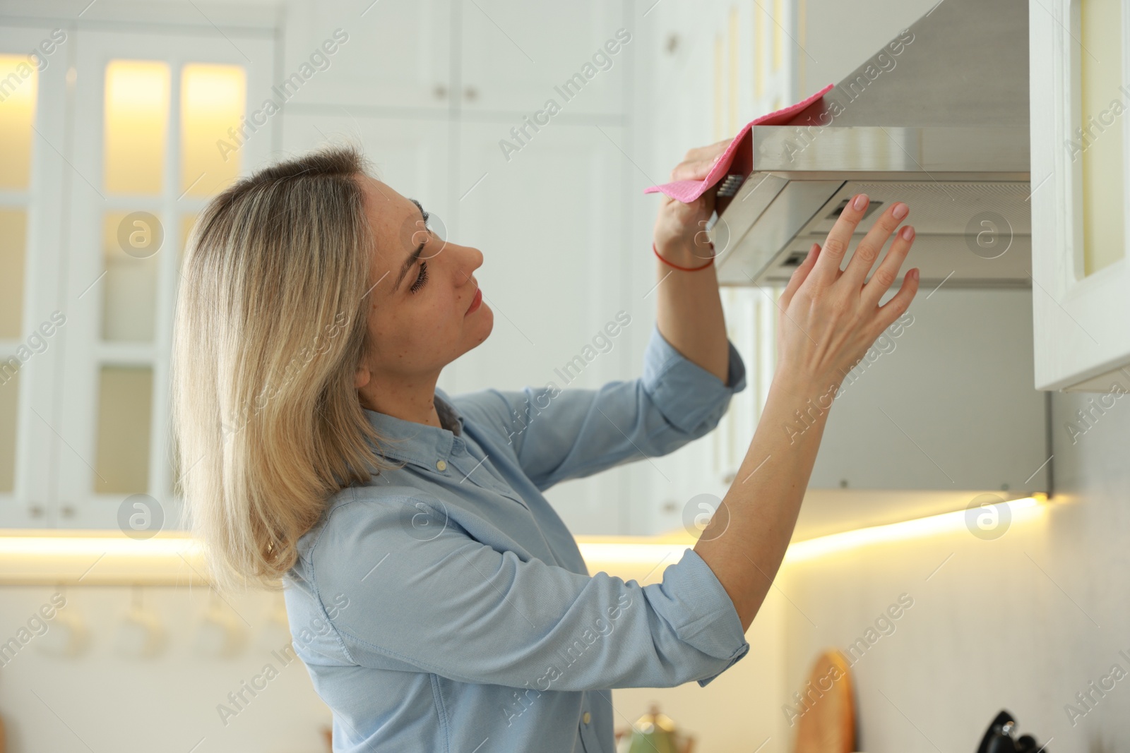 Photo of Woman cleaning kitchen hood with rag indoors