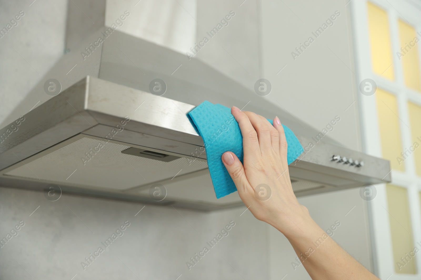 Photo of Woman cleaning kitchen hood with rag indoors, closeup