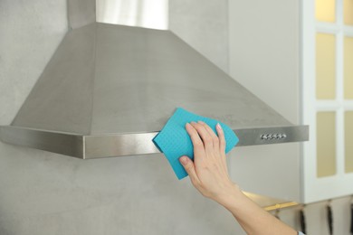 Photo of Woman cleaning kitchen hood with rag indoors, closeup