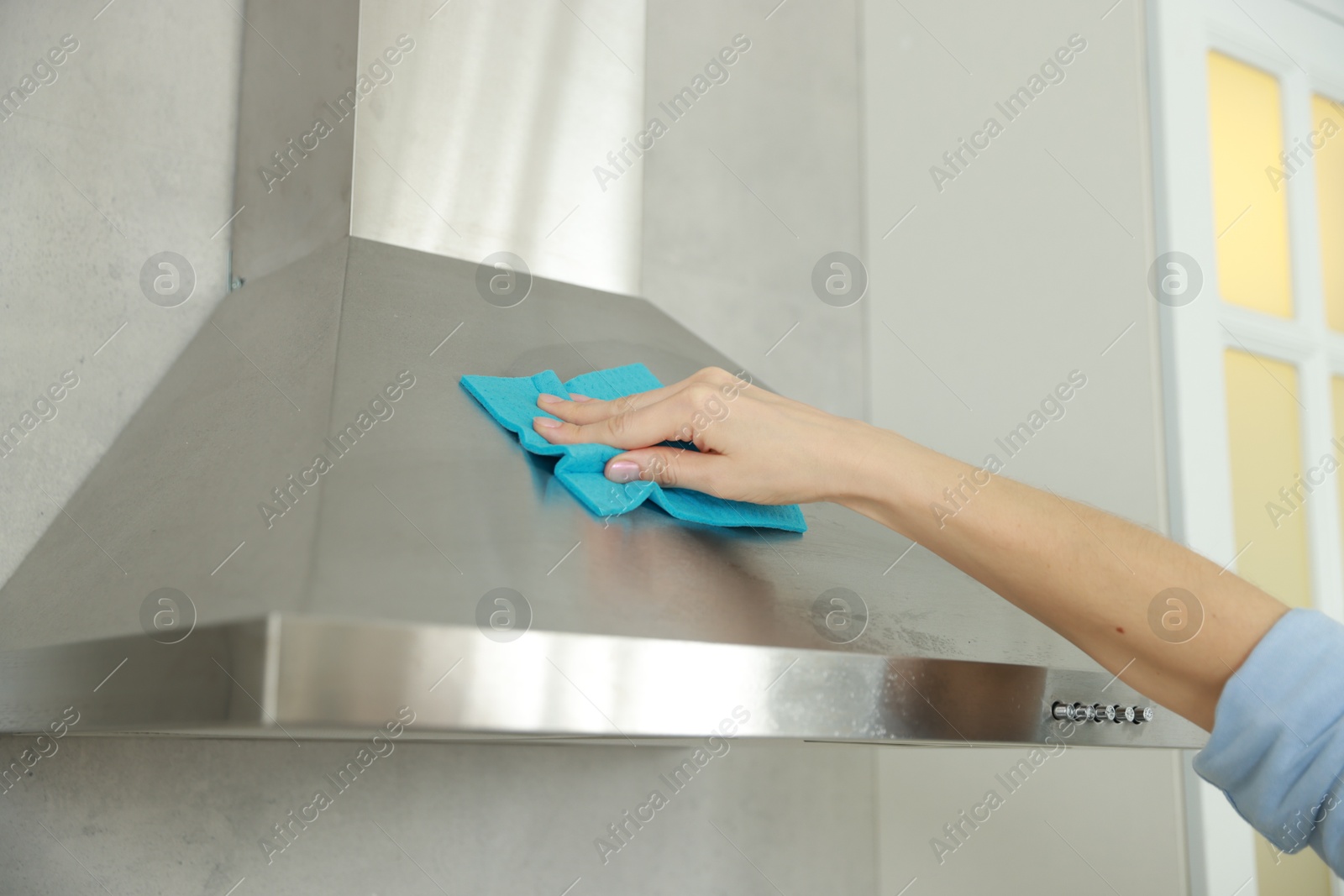 Photo of Woman cleaning kitchen hood with rag indoors, closeup