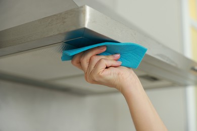 Woman cleaning kitchen hood with rag indoors, closeup