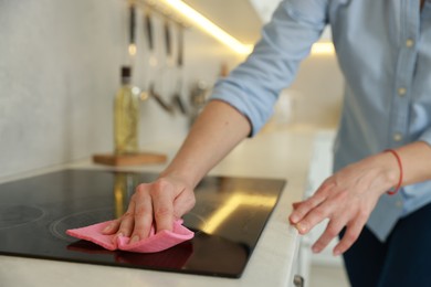 Photo of Woman cleaning induction cooktop with rag indoors, closeup