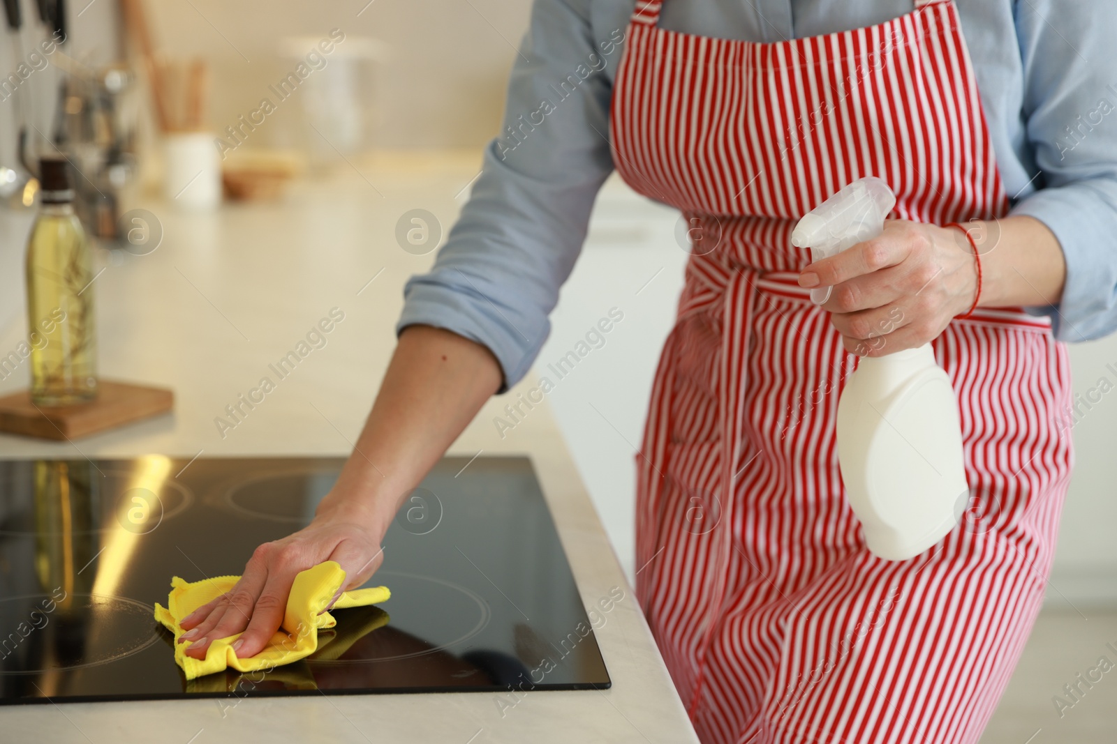 Photo of Woman cleaning induction cooktop with rag and detergent indoors, closeup