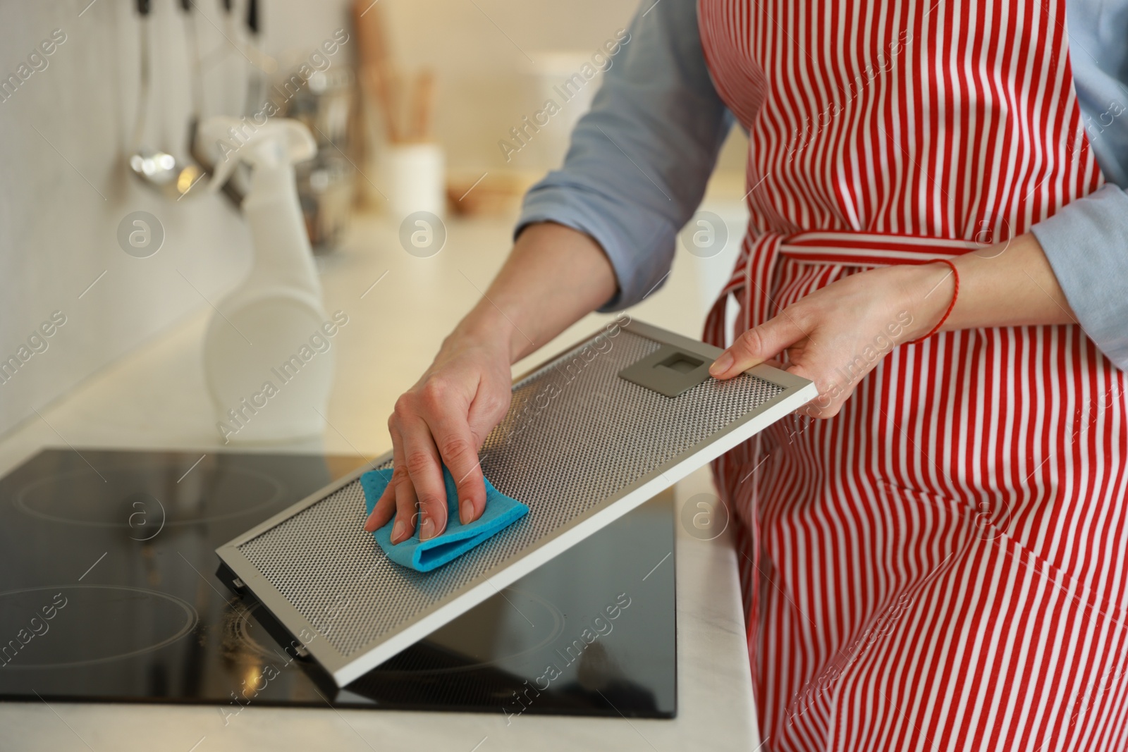 Photo of Woman cleaning filter of kitchen hood with rag indoors, closeup