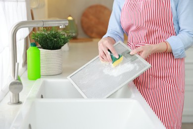 Photo of Woman cleaning filter of kitchen hood with sponge above sink indoors, closeup