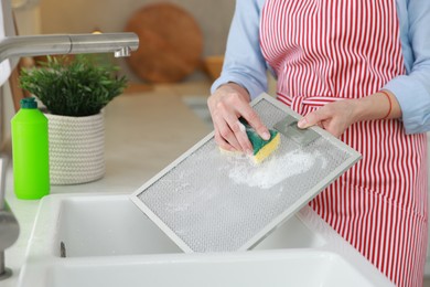 Photo of Woman cleaning filter of kitchen hood with sponge above sink indoors, closeup