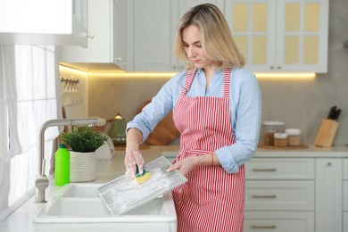 Photo of Woman cleaning filter of kitchen hood with sponge above sink indoors