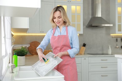 Photo of Woman cleaning filter of kitchen hood with sponge above sink indoors