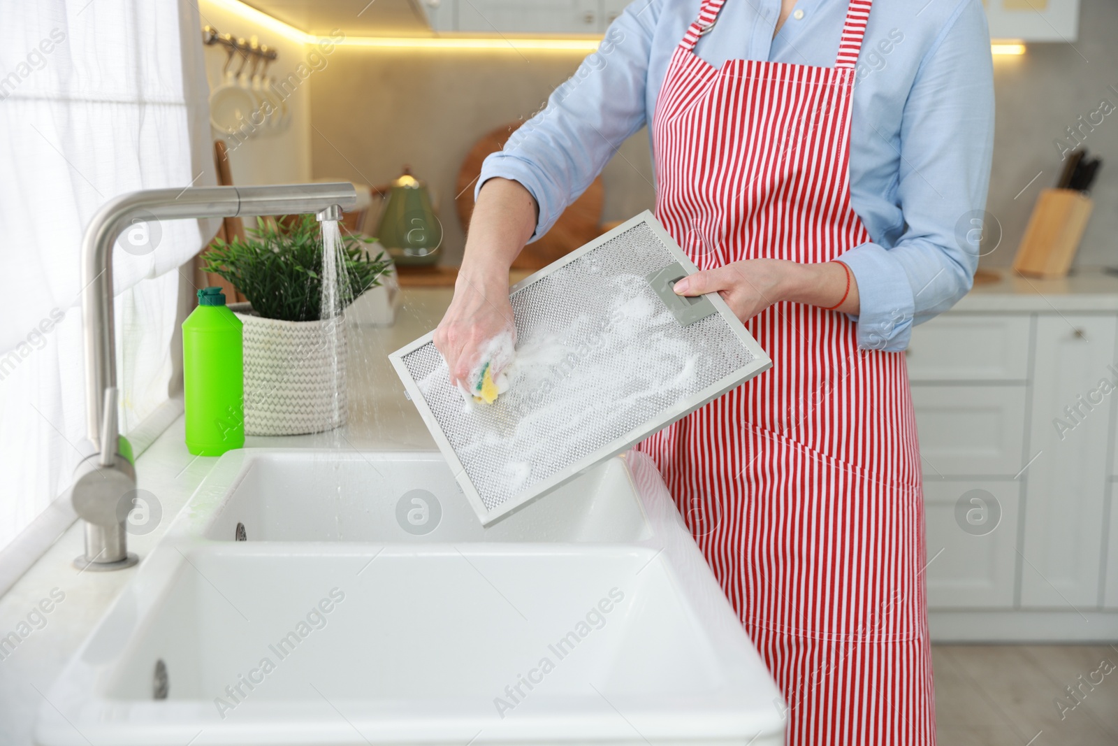 Photo of Woman cleaning filter of kitchen hood with sponge above sink indoors, closeup