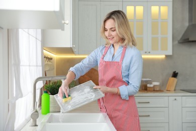 Photo of Woman cleaning filter of kitchen hood with sponge above sink indoors