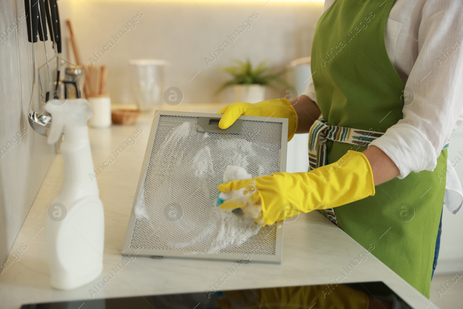 Photo of Woman cleaning filter of kitchen hood with sponge at countertop indoors, closeup