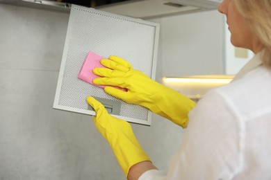 Photo of Woman cleaning filter of kitchen hood with rag indoors, closeup