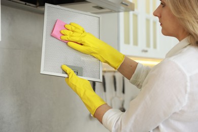 Photo of Woman cleaning filter of kitchen hood with rag indoors, closeup