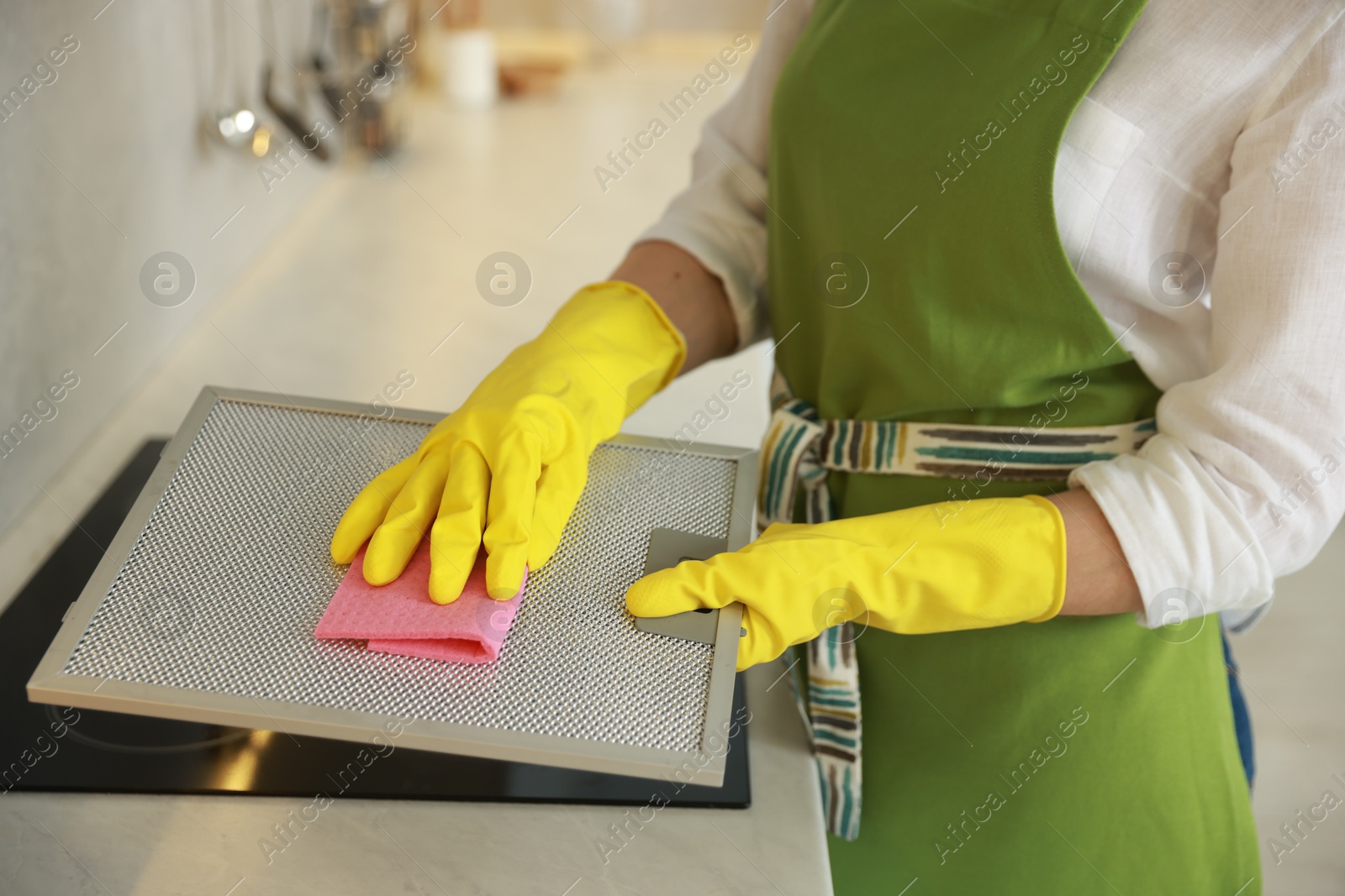 Photo of Woman cleaning filter of kitchen hood with rag indoors, closeup