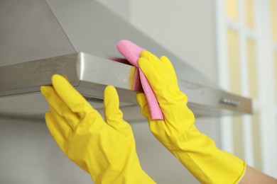 Photo of Woman cleaning kitchen hood with rag indoors, closeup