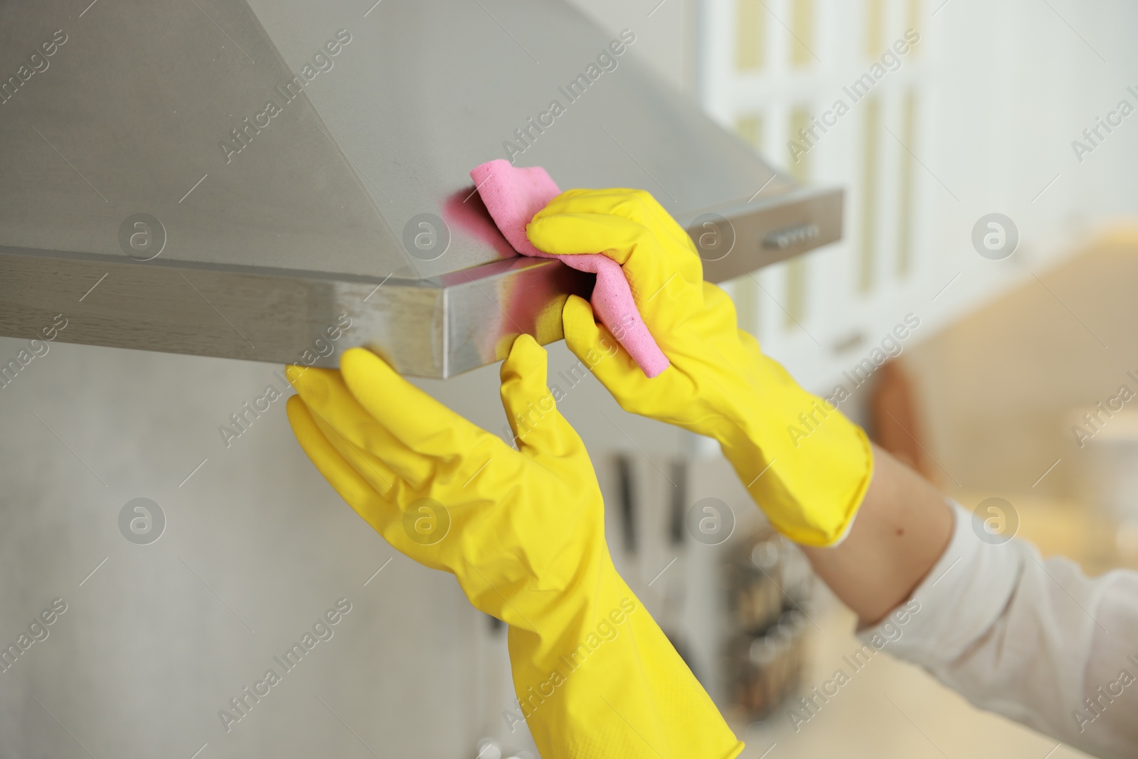 Photo of Woman cleaning kitchen hood with rag indoors, closeup