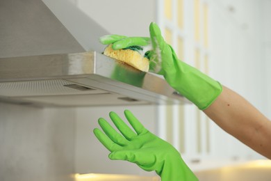 Photo of Woman cleaning kitchen hood with sponge indoors, closeup