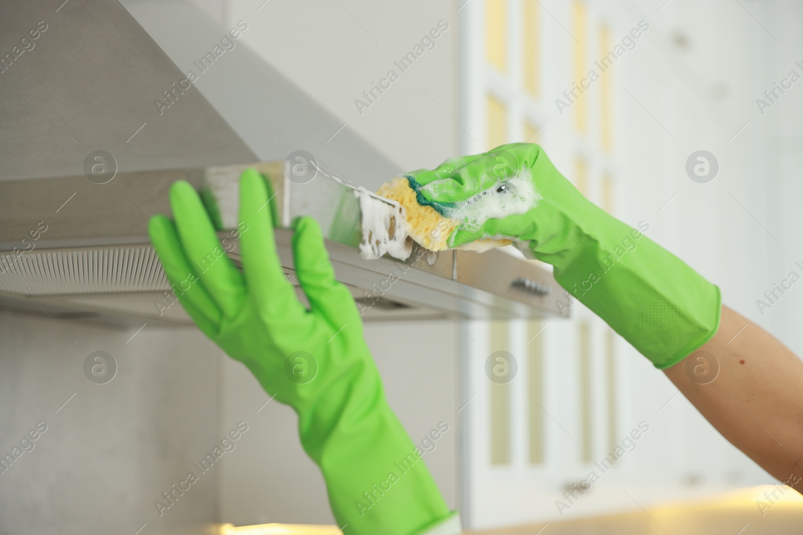 Photo of Woman cleaning kitchen hood with sponge indoors, closeup