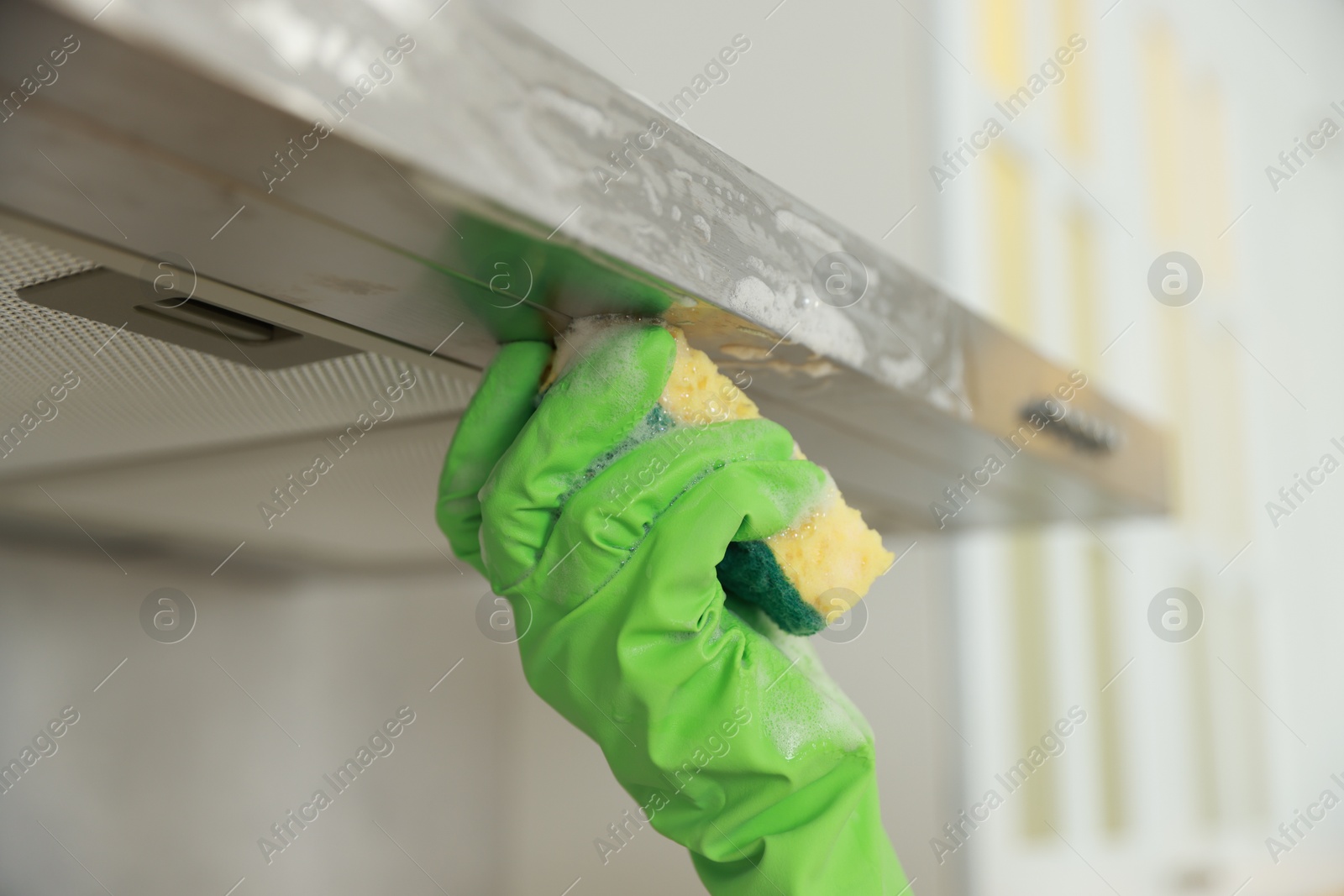 Photo of Woman cleaning kitchen hood with sponge indoors, closeup