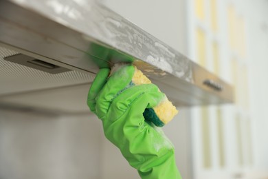 Photo of Woman cleaning kitchen hood with sponge indoors, closeup