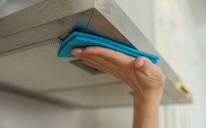 Photo of Woman cleaning kitchen hood with rag indoors, closeup