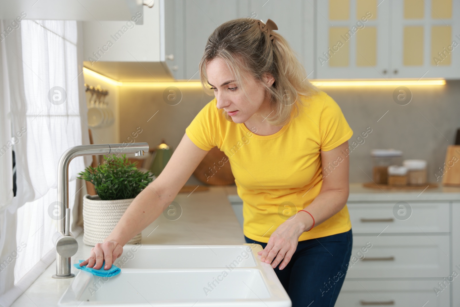 Photo of Woman wiping kitchen sink with rag indoors