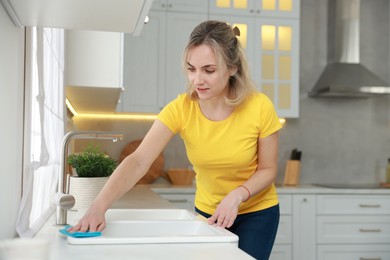 Photo of Woman wiping kitchen sink with rag indoors